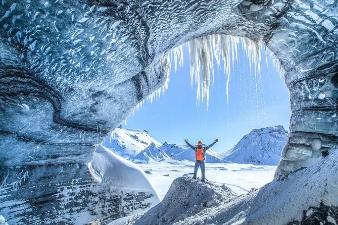 Ein Eishöhlenbogen, der sich im Winter zum Schnee hin öffnet, mit einer Person, die am Eingang die Arme hebt