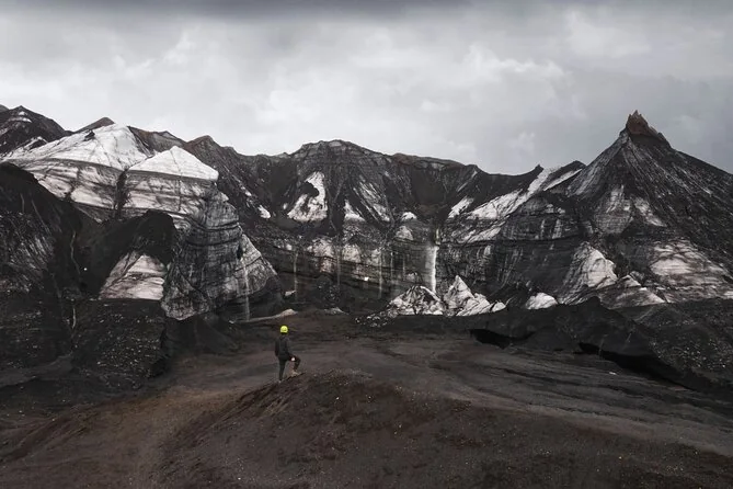 Black ash-covered glacier ridges with a walker crossing them