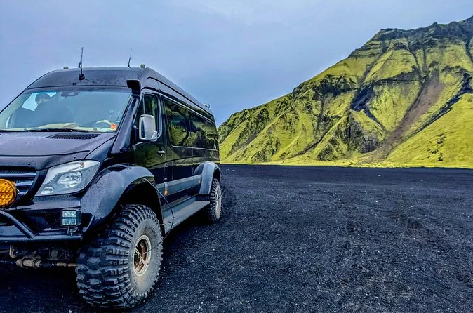 Ein schwarzer 4x4-Transporter auf schwarzem Sand mit einem grünen Berg im Hintergrund