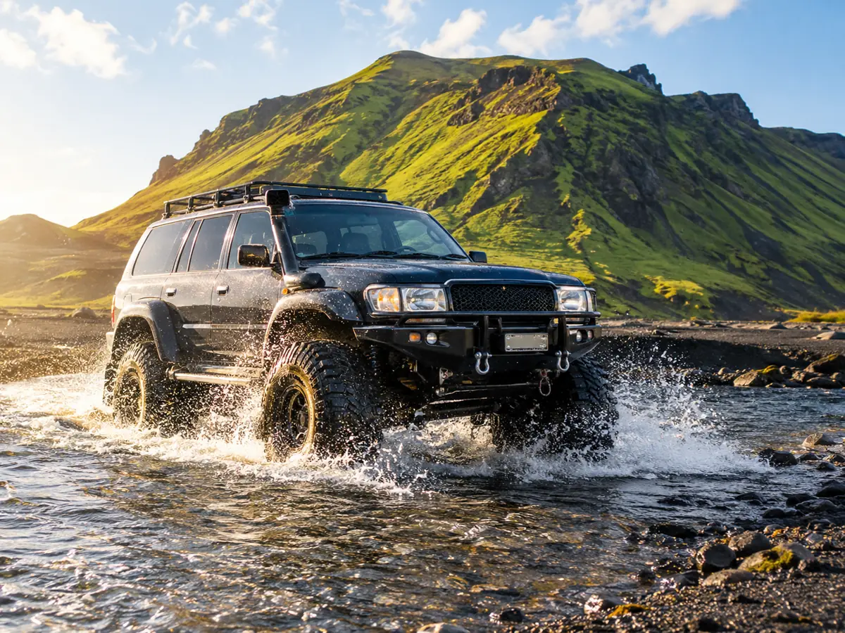 A lifted super jeep with big tyres fording a glacial river on black sand